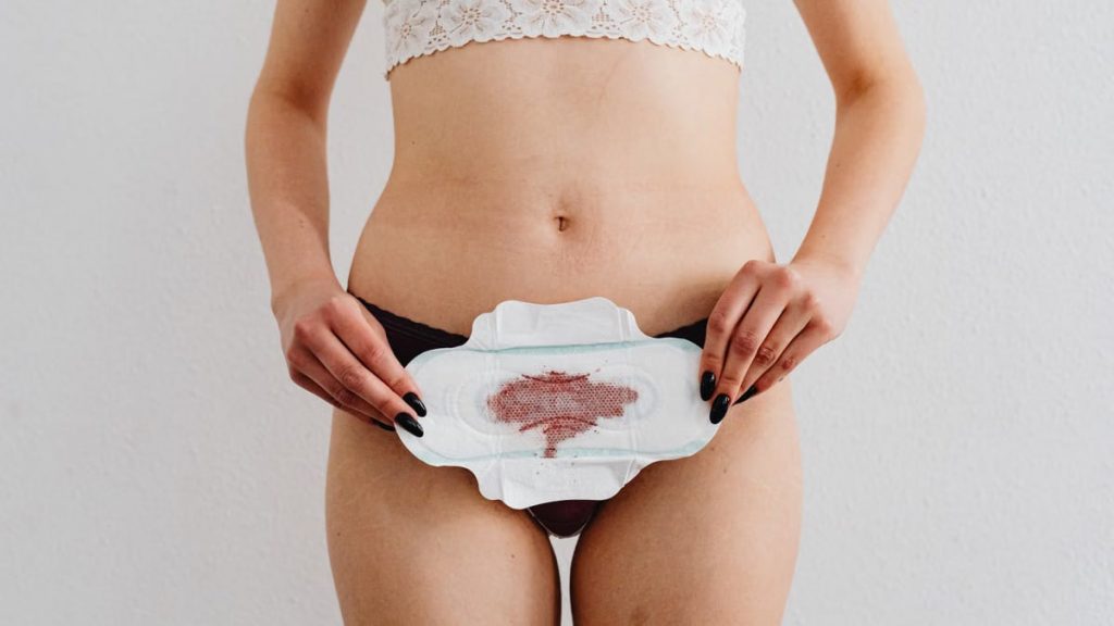 A woman holds a menstrual pad demonstrating feminine hygiene in an indoor setting.