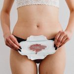 A woman holds a menstrual pad demonstrating feminine hygiene in an indoor setting.