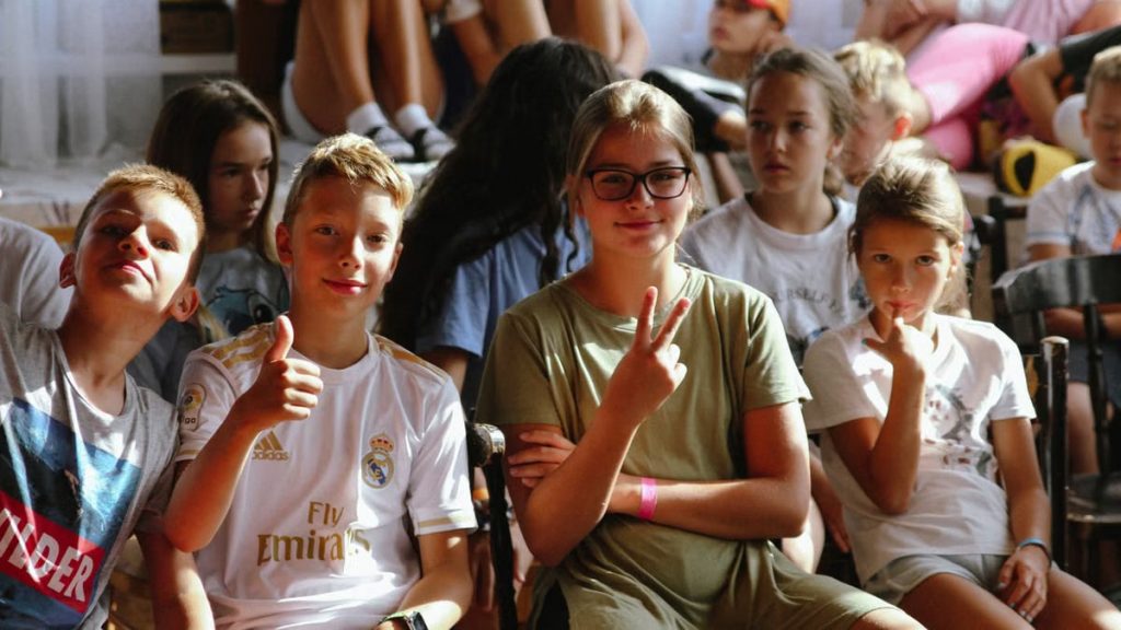 Cheerful group of children sitting together at an indoor event, showcasing friendships and diversity.