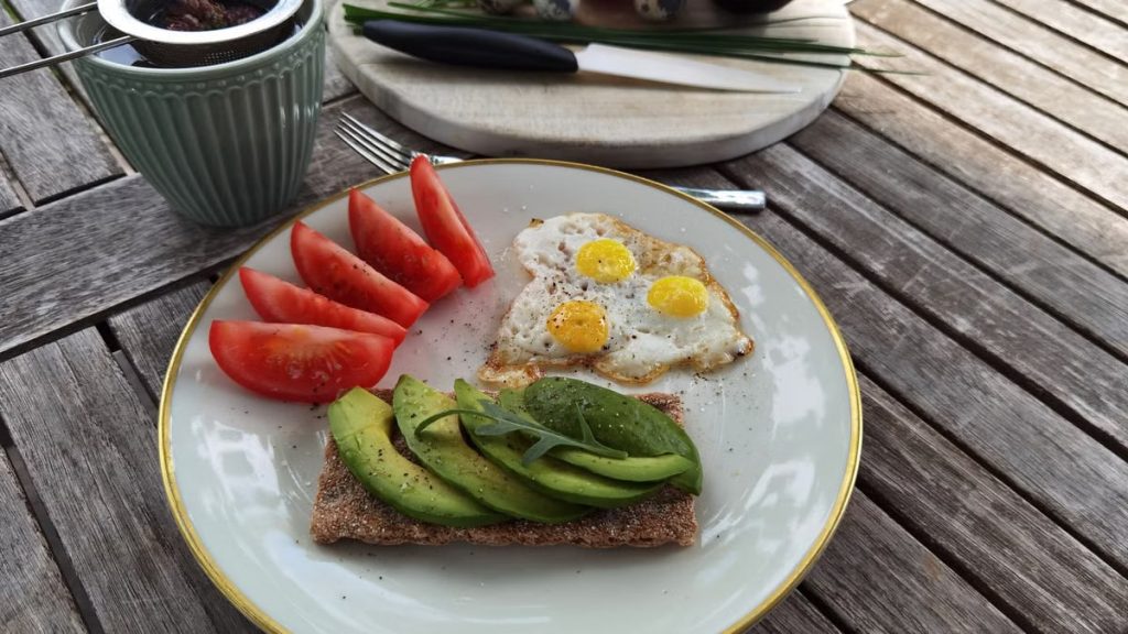 A vibrant outdoor breakfast setup with avocado toast, quail eggs, tomatoes, and tea.