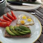 A vibrant outdoor breakfast setup with avocado toast, quail eggs, tomatoes, and tea.