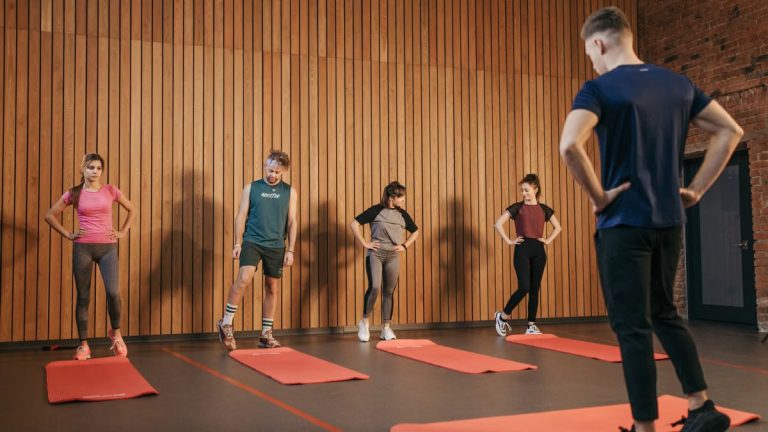 A group exercise class with a personal trainer leading stretching exercises in a gym.